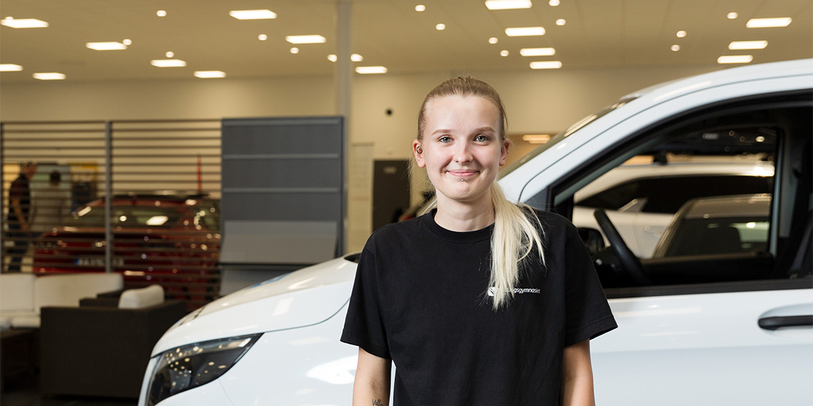 Ung person i motorbranschen på företaget Småländska bil framför en bil.