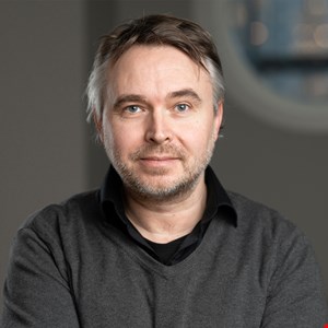 Porträtt av person i mörka kläder mot suddig bakgrund.