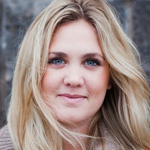 Leende person framför grå stenvägg.