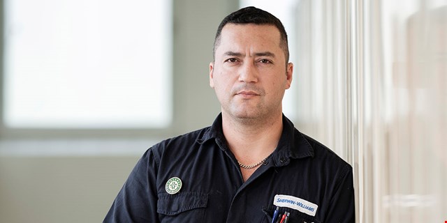 Porträtt av Hans Pacheco, förtroendevald i IF Metall, i arbetskläder med arbetsgivarens logotyp, Sherwin-Williams samt skyddsombudsmärke på bröstet.