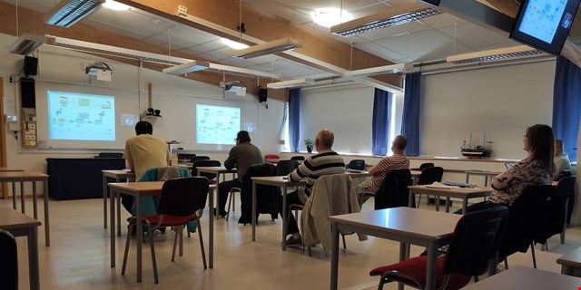 Ett antal personer utspridda i ett stort klassrum med flera skärmar.
