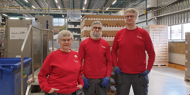 Tre personer med röda arbetskläder i industrimiljö.