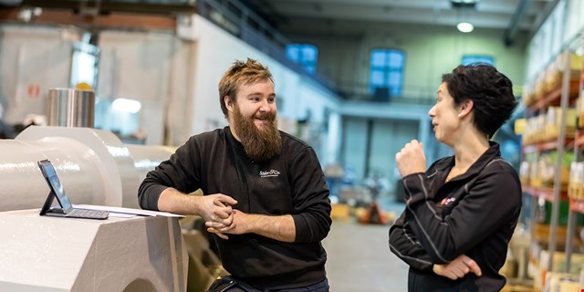 Två personer framför en bärbar dator på en industriarbetsplats.