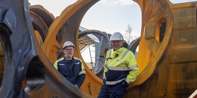 Två personer i arbetskläder intill maskinhus till vindkraftverk