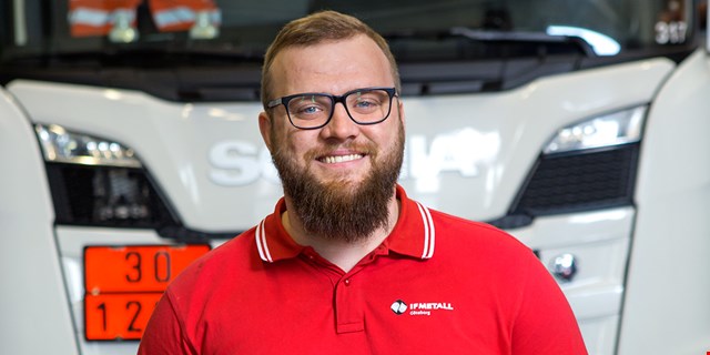 Porträtt av Jim Tellefsdal i röd IF Metall-tröja framför fordon av märket Scania.