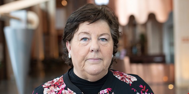 Person i blommig jacka framför suddig bakgrund.