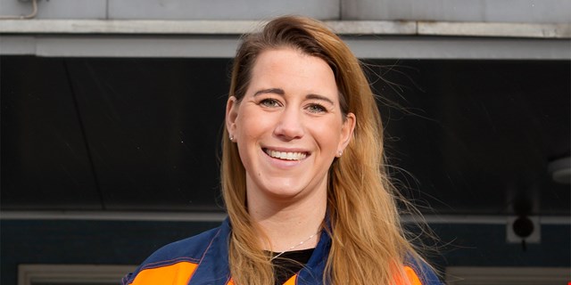 Person i arbetskläder framför industribyggnad.