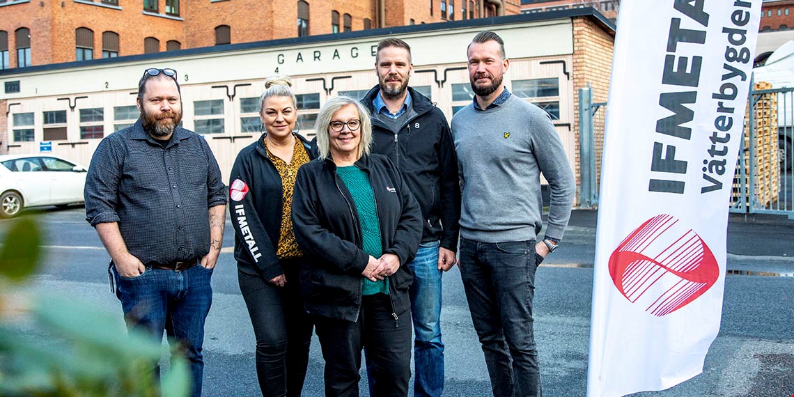 Representanter från klubben med företagsbyggnaden i bakgrunden och en beachflagga där det står IF Metall Vätterbygden på